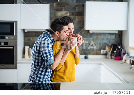 A young couple standing in a kitchen at home, drinking coffee. A young couple standing in a kitchen at home, drinking coffee. 47957511