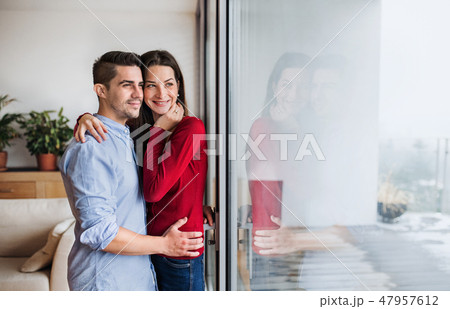 Young couple in love standing by the window at home, hugging. Copy space. 47957612