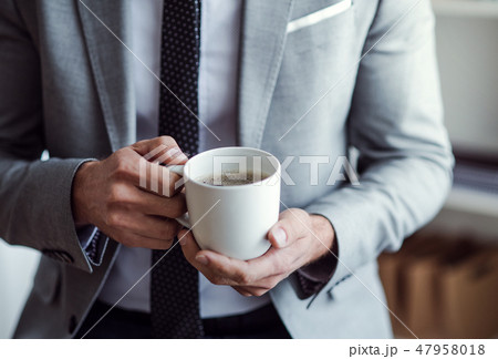 A midsection of businessman standing in an office, holding a cup of coffee. A midsection of businessman standing in an office, holding a cup of coffee. 47958018
