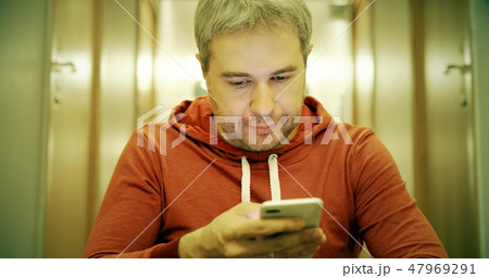 Gray haired young man in casual clothes uses his smartphone in the hallway Gray haired young man in casual clothes uses his smartphone in the hallway 47969291