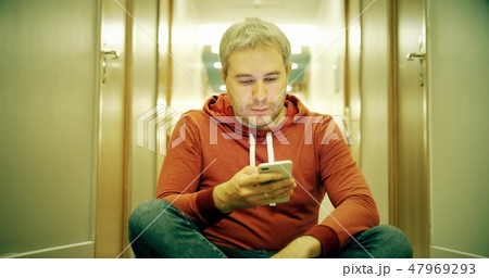 Grey haired young man in casual clothes using his smartphone in the hotel hallway 47969293