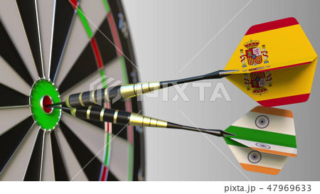 Flags of Spain and India on darts hitting bullseye of the target. International cooperation or 47969633