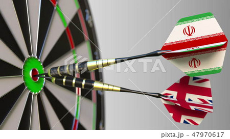 Flags of Iran and the United Kingdom on darts hitting bullseye of the target. International 47970617