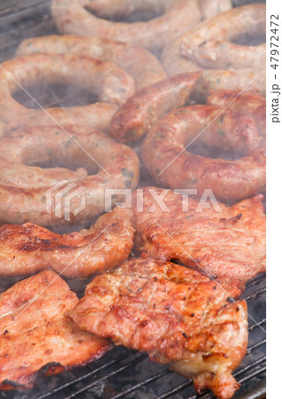 Grilled sausage and pork cooking on flaming grill. 47972472