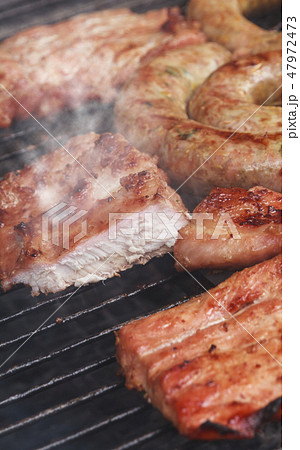 Grilled sausage and pork cooking on flaming grill. 47972473
