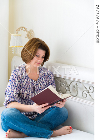 Woman reading a book sitting on bed in the bedroom Woman reading a book sitting on bed in the bedroom 47972792