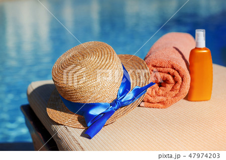 Orange cotton towel and sunscreen body lotion and hat in a orange tube on the background pool. Means 47974203