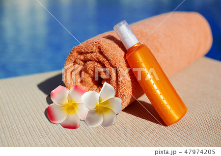 Orange cotton towel and sunscreen body lotion in a orange tube on the background pool. Means for 47974205