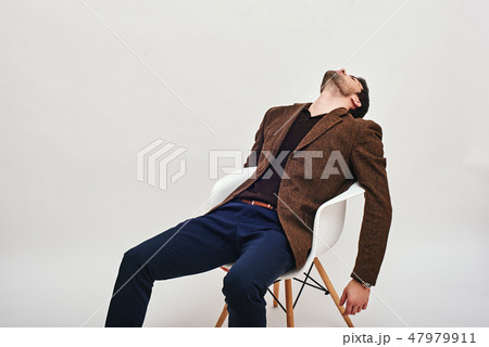 Sick and tired. Stylish dark-haired businessman sitting on a chair, leaning back and looking at the 47979911