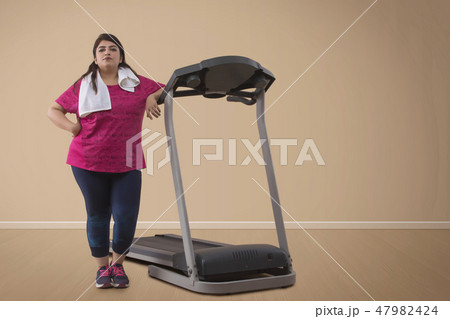 Overweight woman standing with treadmill Overweight woman standing with treadmill 47982424