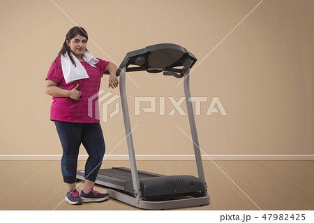 Overweight woman standing with treadmill Overweight woman standing with treadmill 47982425