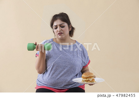 Sad Overweight Woman holding a burger and dumbbell 47982455