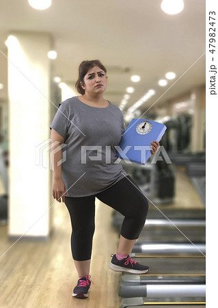 fat woman in a gym holding a weight scale fat woman in a gym holding a weight scale 47982473