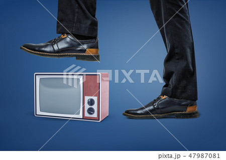 A giant businessman's leg stepping on a small retro TV box with an empty screen. 47987081