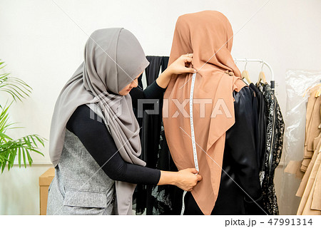 Female Muslim designer measuring back of customer 47991314