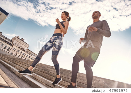 Exercising on fresh air. Portrait of a young sports couple doing morning workout on a sunny and warm Exercising on fresh air. Portrait of a young sports couple doing morning workout on a sunny and warm 47991972