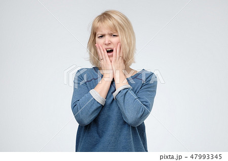 Blonde young woman in blue shirt with shocked face Blonde young woman in blue shirt with shocked face 47993345