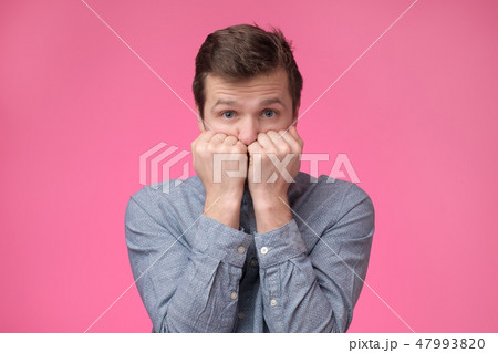 Man looks scared in the camera and presses his fists to his mouth in a sign of fear and fright. Man looks scared in the camera and presses his fists to his mouth in a sign of fear and fright. 47993820