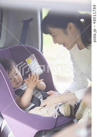 子どもをチャイルドシートに座らせる母親の写真素材