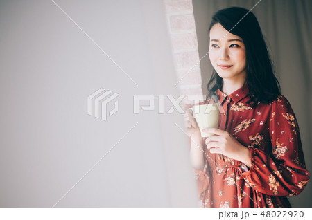 マグカップを手に窓際に立つ女性 48022920