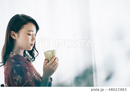 マグカップを手に椅子に座る赤いワンピースの女性 48022965