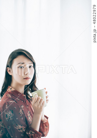 マグカップを手に椅子に座る赤いワンピースの女性 マグカップを手に椅子に座る赤いワンピースの女性 48022979