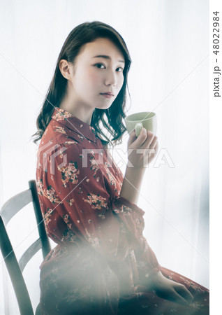 マグカップを手に椅子に座る赤いワンピースの女性 48022984