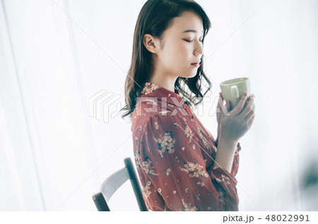マグカップを手に椅子に座る赤いワンピースの女性の写真素材