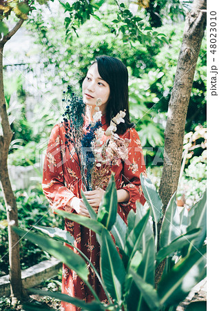 庭で花束を持つ赤いワンピースの女性 48023010