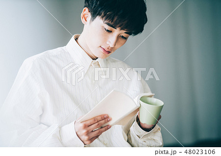 窓際で本を読む白いシャツの男性 48023106