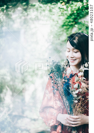 庭で花束を持つ赤いワンピースの女性 48023107