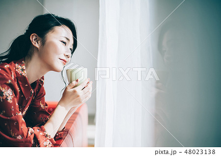 窓際のソファに座る髪をアップにした赤いワンピースの女性 48023138