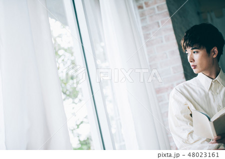 窓際で本を読む白いシャツの男性 48023161