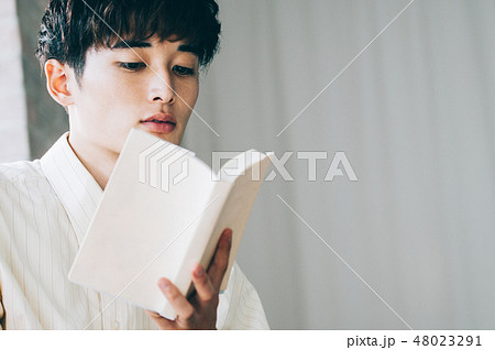 窓際で本を読む白いシャツの男性の写真素材