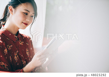 窓際のソファに座り本を読む髪をアップにした赤いワンピースの女性 48023292