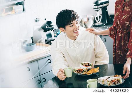 テーブルにつく男性にサンドイッチを運ぶ女性 48023320