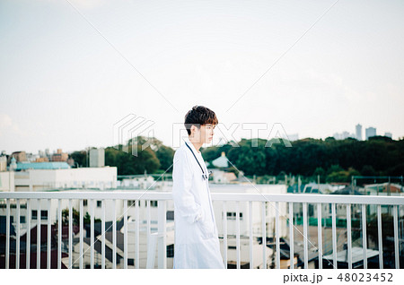 屋上で手すりにもたれる白衣を着た男性の写真素材