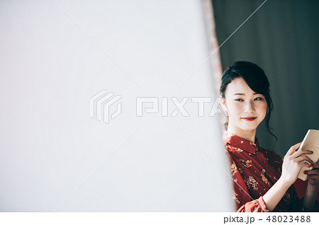 窓際のソファに座り本を読む髪をアップにした赤いワンピースの女性の写真素材