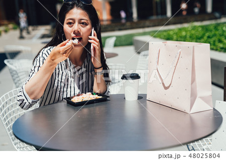 asian woman talking on smart phone eating salad 48025804