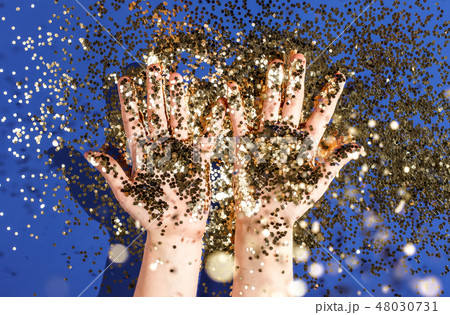 Hands of a child in gold glittering confetti on a blue background, top view. Birthday and holiday Hands of a child in gold glittering confetti on a blue background, top view. Birthday and holiday 48030731