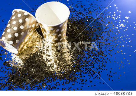 Golden paper cups for birthday party with golden confetti on blue background Golden paper cups for birthday party with golden confetti on blue background 48030733