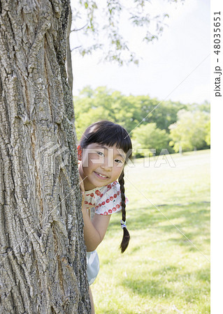 木の陰から顔を出す子供の写真素材