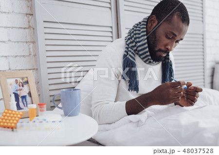 Serious international male looking at thermometer Serious international male looking at thermometer 48037528
