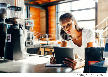 Cafe owner leaning on counter making notes in cafe Cafe owner leaning on counter making notes in cafe 48051978