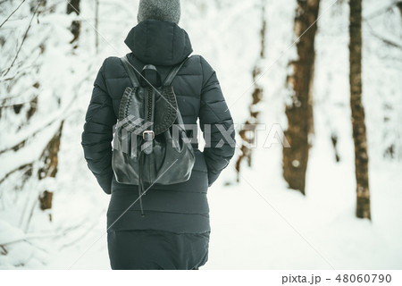 a back shot of a Beautiful youngwoman dressed in a black winter jacket with leather backpack walks 48060790