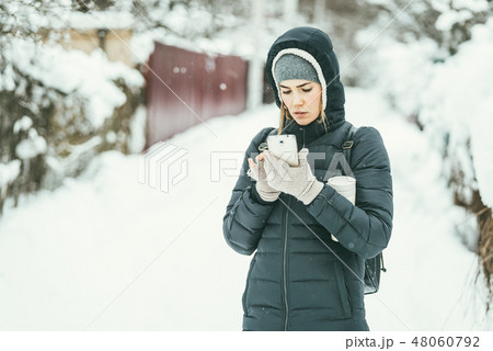 Beautiful woman dressed in a black winter jacket with mobile phone and thermos flask under her arm 48060792