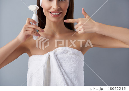 Joyful young woman holding pore cleansing brush and pointing at it 48062216