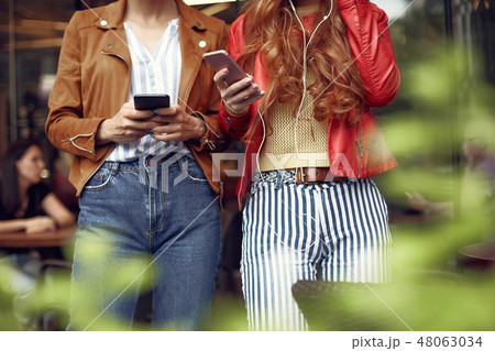 Two stylish young women using cellphones outdoors Two stylish young women using cellphones outdoors 48063034