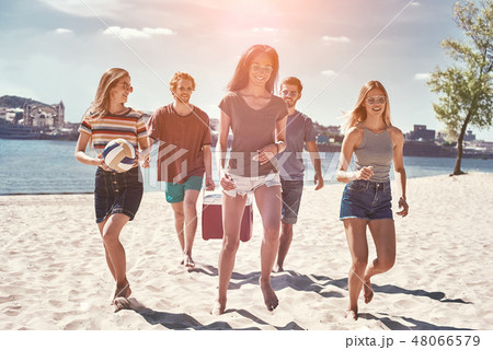 Friends on the beach. Rear view of cheerful young people walking by the beach to the sea while two 48066579