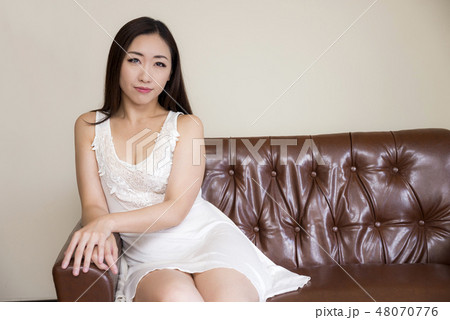 ソファに座って肘掛に手を置く白いワンピースの女性の写真素材